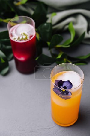 Artistic presentation of two colorful cocktails adorned with edible flowers, set against a chic gray surface