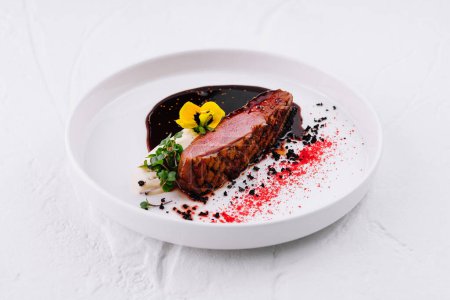 Elegant plated beef steak with a rich red wine sauce, garnished with edible flowers on a white background