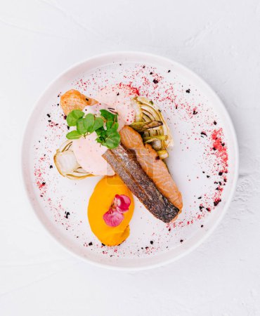 Vue de dessus d'un délicieux filet de saumon plaqué avec des légumes vibrants et de la sauce sur un fond blanc
