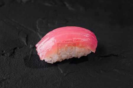 Zbliżenie świeżego kawałka sushi z tuńczyka nigiri na teksturowanym czarnym tle łupkowym