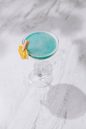 Refreshing blue cocktail in a martini glass, accented with an orange twist, presented on a chic marble countertop