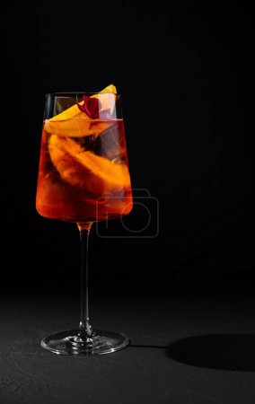 Vibrant aperitif cocktail in a stemmed glass with orange slices, against a dark background