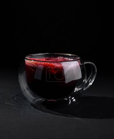 A modern double-walled glass cup filled with red tea, isolated on a dark, moody backdrop
