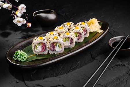 Elegant sushi arrangement with chopsticks and soy sauce jug on a dark, slate surface