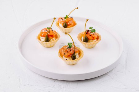 Delicious tartlets filled with smoked salmon and garnish on a sleek white plate