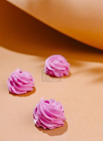 Three delicate pink meringue swirls artistically placed on a warm peach-colored backdrop