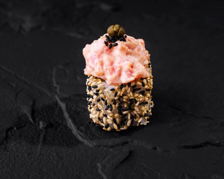 Artfully presented spicy tuna sushi roll garnished with sesame seeds on a dark slate background