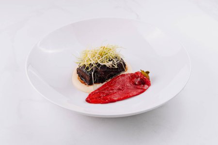 Elegant dish of tender braised beef on a smear of puree with a vibrant red vegetable garnish on a white plate