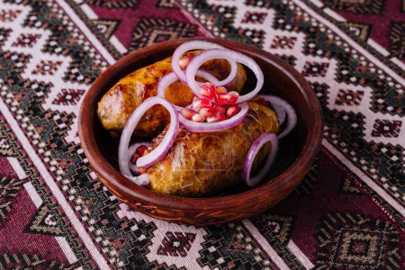 Shkmeruli, un plato de pollo georgiano en un tazón rústico, adornado con cebollas y semillas de granada