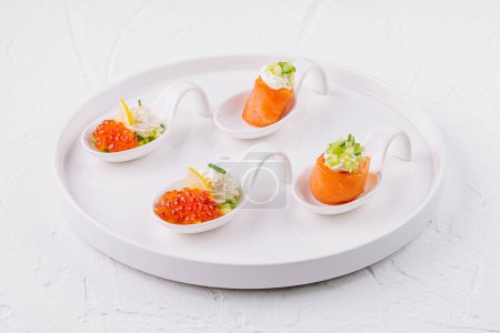 Photo for White ceramic platter with gourmet salmon and caviar appetizers on a bright background - Royalty Free Image
