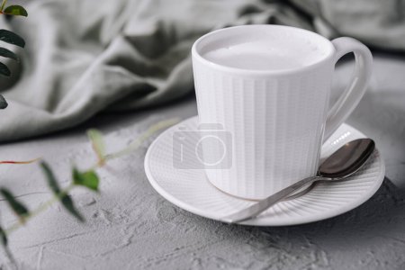 Enjoying a cozy morning with a frothy milk cappuccino in a simple and elegant white cup on a textured table surrounded by green leaves, creating a tranquil and relaxing coffee break atmosphere