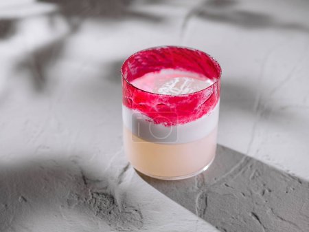 Cocktail élégant avec des couches roses et blanches vibrantes, présenté sur un fond moderne et texturé
