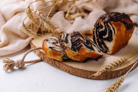 Pan de remolino de semillas de amapola recién horneado presentado en una tabla de madera rústica con espigas de trigo