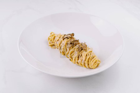 Elegant serving of spaghetti topped with shaved truffles on a sleek plate, marble background