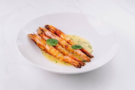 Sukkulente gegrillte Garnelen mit einer Knoblauchbutter-Sauce garniert mit frischem Basilikum, serviert auf einem modernen weißen Teller