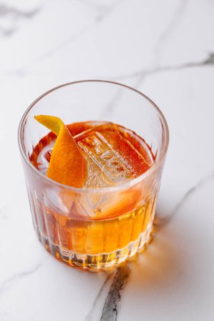 Close-up of a classic old fashioned cocktail garnished with a fresh orange twist on a marble surface