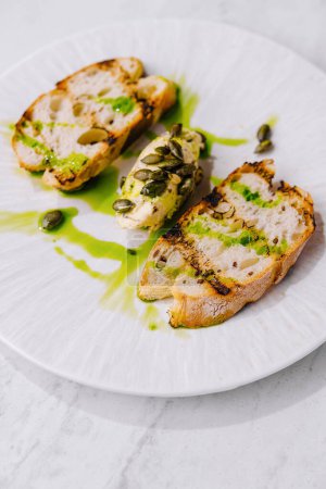 Elegant plating of avocado toast with capers and drizzle of herb oil on a white dish