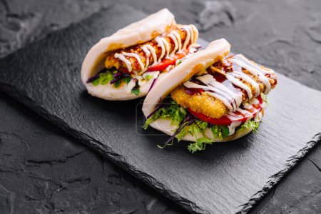 Delicious chicken burger with fresh toppings and sauces on a dark slate background