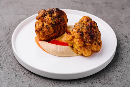 Gourmet cauliflower steaks with a vibrant red sauce, elegantly presented on a modern plate