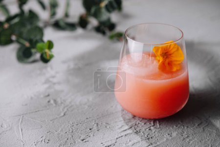 Stylish glass of blush cocktail decorated with a vibrant edible flower, on a textured surface