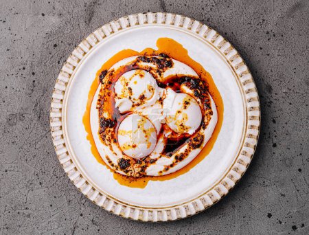 Foto de Vista superior de deliciosos huevos escalfados rociados con una salsa picante, servidos en un plato blanco adornado - Imagen libre de derechos