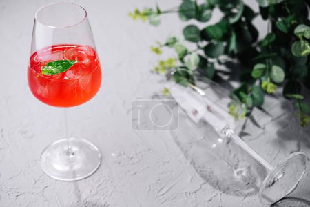 Elegant glass of vibrant red summer cocktail adorned with fresh mint on a textured surface