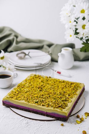 Delicioso pastel de pistacho emparejado con café en una mesa blanca, complementado con flores frescas