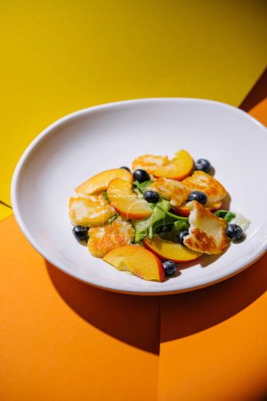 Halloumi- und Pfirsichsalat mit Blaubeeren auf weißem Teller mit zweifarbigem Hintergrund