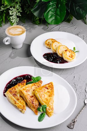 Delicious crepes with berry syrup accompanied by cheese pancakes and a cup of coffee