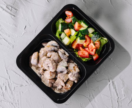Healthy chicken breast with creamy sauce and fresh garden salad in meal prep boxes