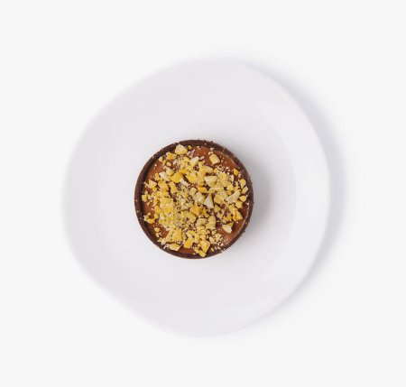 Top view of a single chocolate tart topped with crushed nuts on a clean white plate