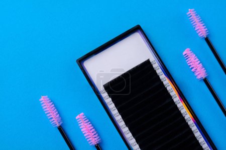 Top view of eyelash extension set with pink brushes on a vivid blue backdrop