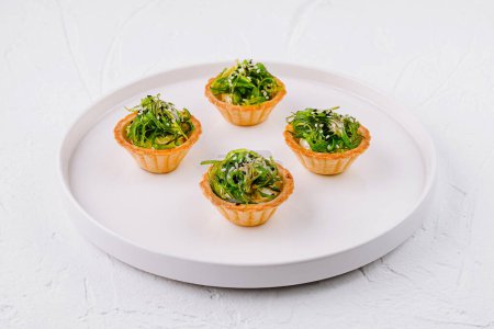 Élégant apéritif, salade d'algues en coquilles acidulées, servi sur une assiette blanche moderne
