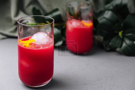 Two glasses of vibrant red citrus cocktail with ice, garnished with lemon zest