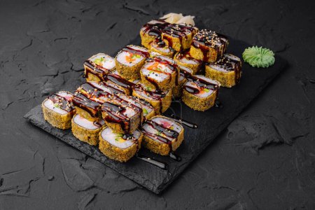 Różnorodność bułek sushi ozdobionych sosem i sezamem na eleganckim czarnym łupku, gotowych na posiłek dla smakoszy