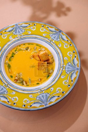 Vue du haut vers le bas d'un bol coloré avec de la soupe crémeuse à la citrouille, garnie de graines et de croûtons