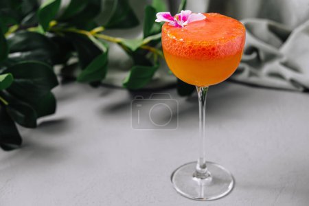 Classy tropical cocktail beautifully garnished with a pink flower placed on a modern surface