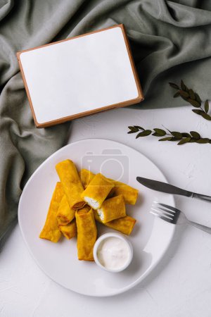 Photo for Delectable plate of spring rolls beside a bowl of dipping sauce on a sophisticated table draped with a green cloth - Royalty Free Image