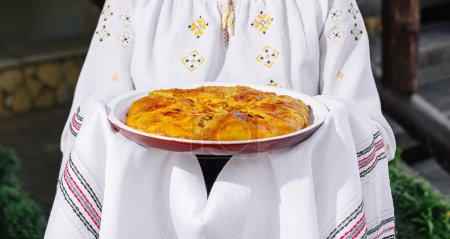 Person in folk costume holds a homemade pie, showcasing cultural cuisine