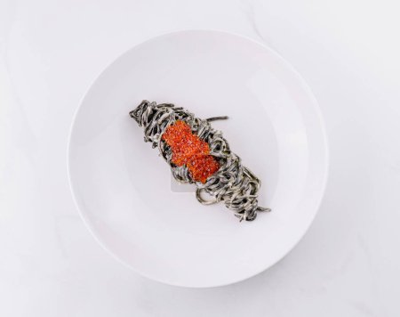 Elegant presentation of squid ink pasta topped with luxurious red caviar on a white plate