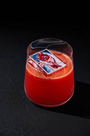 Cóctel rojo vibrante con un cubo de hielo transparente, servido en un elegante vaso sobre un fondo oscuro y malhumorado