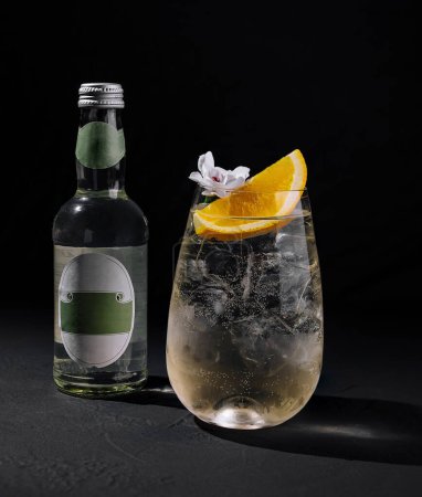 Refrescante gin tonic servido con hielo, guarnición de naranja, y una flor en un elegante vaso al lado de una botella