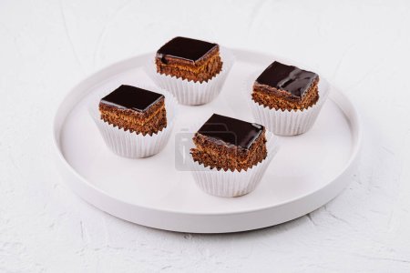 Delicious mini cakes with chocolate glaze, presented on a white plate against a textured background