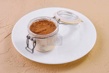 Tiramisu, traditional Italian dessert in a glass presented on a white dish with a textured background