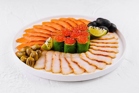 Photo for Vibrant platter featuring smoked salmon, fish slices, red caviar, olives, and lime on a white background - Royalty Free Image
