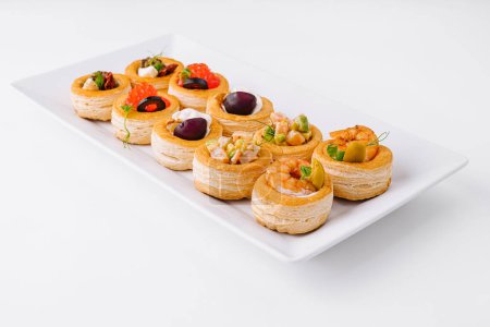Photo for Selection of elegant mini tartlets with savory toppings on a sleek white platter - Royalty Free Image