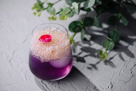 Sophisticated cocktail with purple hue and delicate flower garnish, on a textured surface