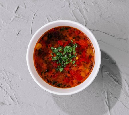 Top view of a colorful vegetable soup garnished with fresh herbs in a bowl on a textured background