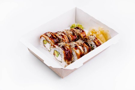 Tasty eel sushi roll with avocado and sesame seeds in a paper takeout container, isolated on white