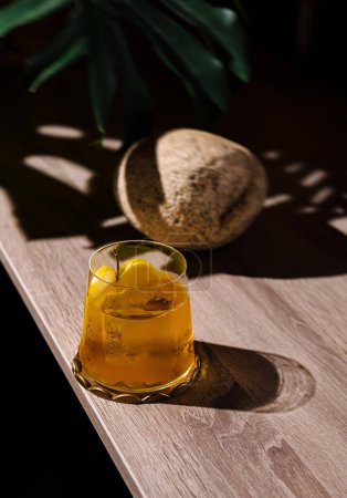 Eiskaltes Getränk mit Zitronengarnitur auf einem Holztisch, mit Pflanzenschatten